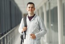 Estudante de medicina com jaleco branco e mochila nas costas parado em um corredor. Imagem ilustra como conseguir o FIES para Medicina em 2023.