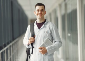 Estudante de medicina com jaleco branco e mochila nas costas parado em um corredor. Imagem ilustra como conseguir o FIES para Medicina em 2023.