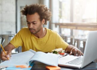 Inscrição para o FIES 2023: jovem negro sentado na mesa de frente para um notebook usa o computador para estudos.