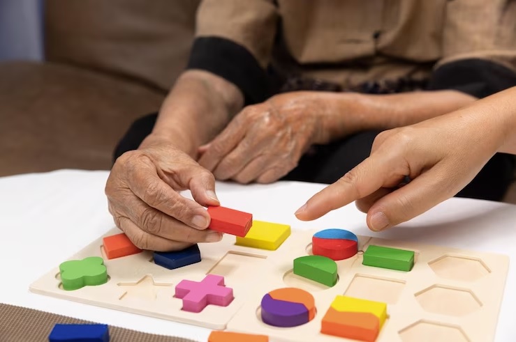 Psicomotricista e paciente idoso trabalham atividades para fortalecer habilidades motoras com as mãos.